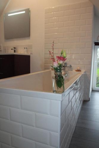 a white bathroom with a tub with a vase of flowers on it at La Catiniere in Arnage