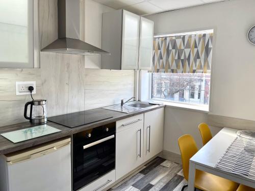 a kitchen with white cabinets and a sink and a table at The Bawdens Holiday Apartments in Blackpool