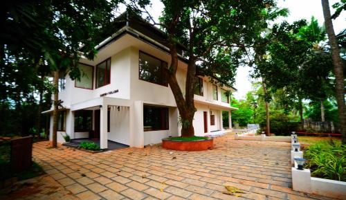 a white house with a tree in front of it at Hortus Malabaricus Garden Resort in Cheruthuruthi