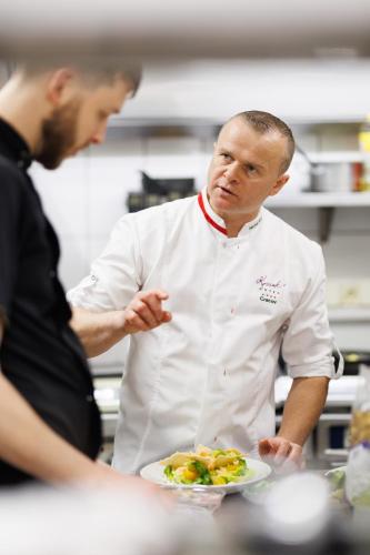 a chef standing in a kitchen with a plate of food at Hotel Kossak in Kraków
