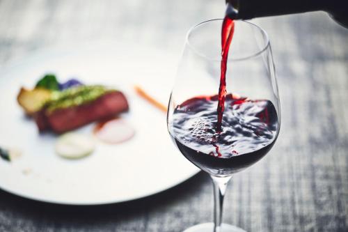 a glass of red wine with a plate of food at Hotel Indigo Nagasaki Glover Street by IHG in Nagasaki