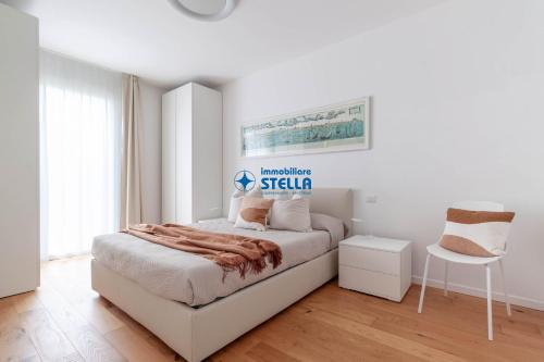 a white bedroom with a bed and a chair at Wave Island in Lido di Jesolo