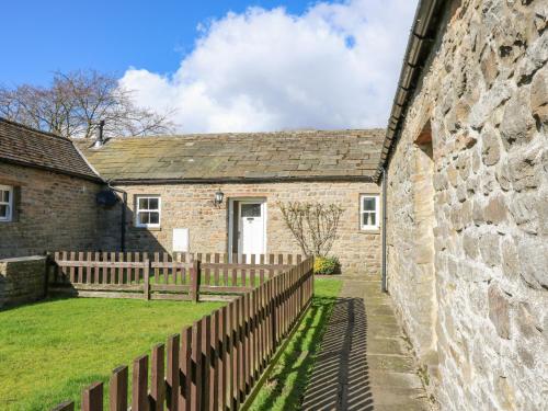 a stone house with a wooden fence next to a wall at Pencroft Cottage in Leyburn