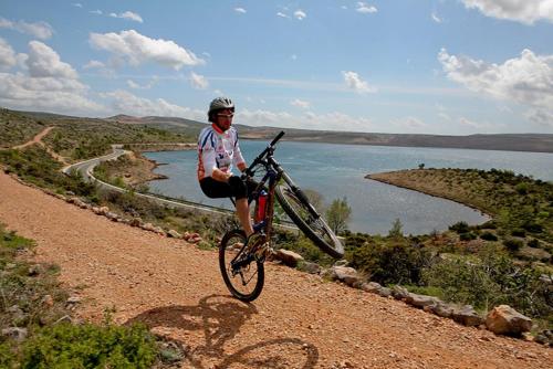 a man riding a bike on a dirt road next to a lake at Rooms & Pansion Odmor in Rovanjska