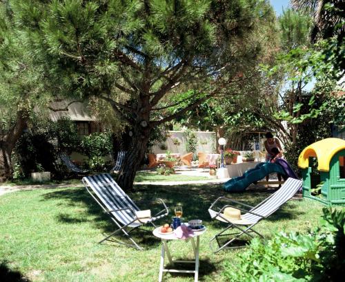 a woman sitting in a yard with two chairs and a table at Hôtel Le Mirage in Saintes-Maries-de-la-Mer