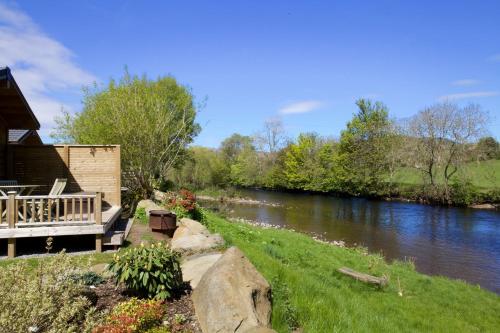 a house with a deck next to a river at Braidhaugh Holiday Lodge and Glamping Park in Crieff