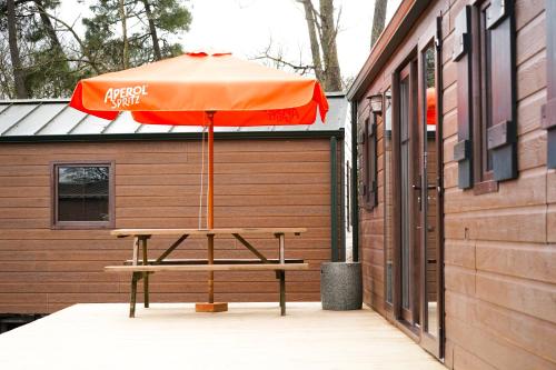 une table de pique-nique avec un parasol orange à côté d'un bâtiment dans l'établissement Pôle Européen du Cheval - Les Cottages de la Futaie, à Yvré-lʼÉvêque