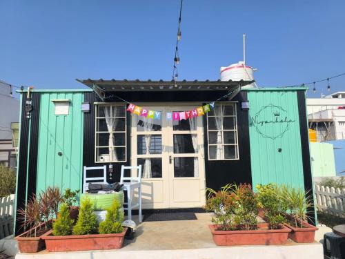 a tiny house with green and white doors and plants at Cozy Cottage near Hessarghatta in Bengaluru