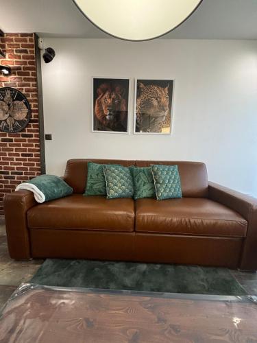 a brown leather couch in a living room with pictures at Evasion Verdoyante Vue sur jardin avec balcon et parking in Montigny-le-Bretonneux