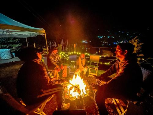 Un groupe de gens assis autour d'un feu la nuit dans l'établissement The Elevia, Jibhi, à Jibhi