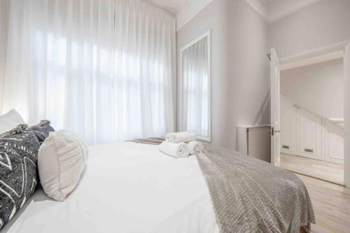 a white bedroom with a large white bed with towels on it at 2BR, garden, 60" TV with sound system in London