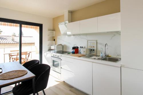 une cuisine avec des armoires blanches et une table et une salle à manger dans l'établissement JULES GREC Appartement Loggia Piscine et Confort à Antibes, à Antibes