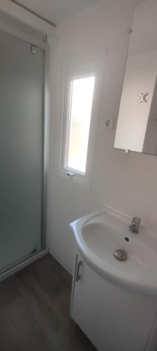 une salle de bain blanche avec un lavabo et une fenêtre dans l'établissement Mobile home A32, à Sérignan