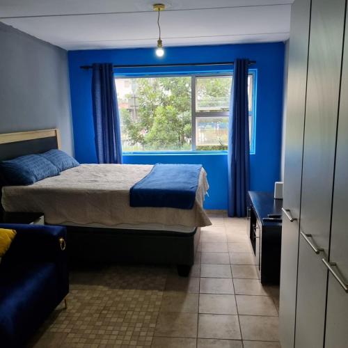 a bedroom with blue walls and a bed with a window at Greggs Place at Capital Hill Arcadia in Pretoria
