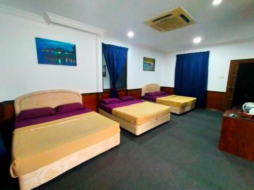 three beds in a room with blue curtains at Capital O 91118 Chalet Seri Idaman in Kampong Batu Maung