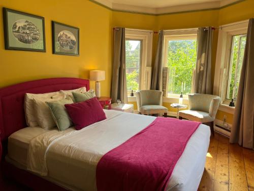 a bedroom with a large bed and two windows at La Belle Victorienne in Magog-Orford