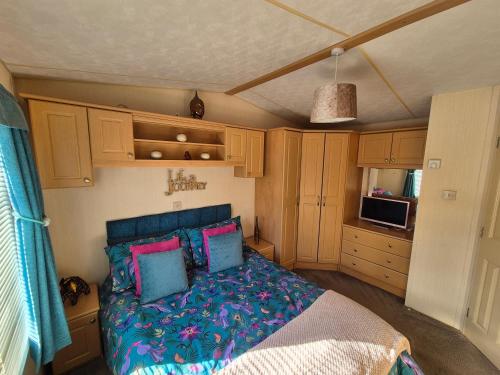 a bedroom with a bed with blue and pink pillows at 24 The Beeches Caravan Park in Gilcrux