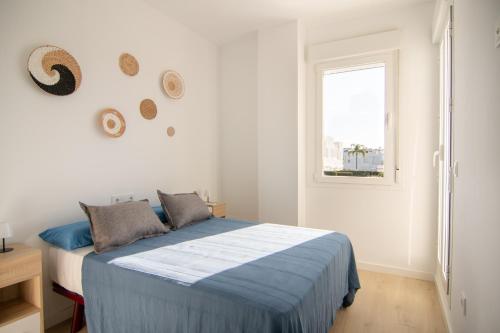 a white bedroom with a blue bed and a window at Casa PLAYA FONTANILLA in Conil de la Frontera