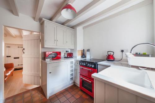 a kitchen with white cabinets and a red stove top oven at Cosy Cottage in the Heart of Charnwood Forest in Woodhouse