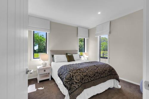 a white bedroom with a bed and two windows at Peter's Puketaha Homestay in Ruakura Junction