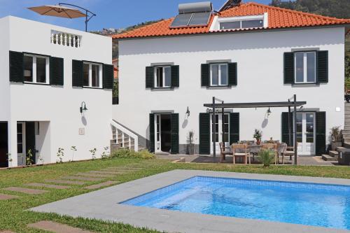 a villa with a swimming pool in front of a house at Casa das Rosas e Casa Do Mar in Arco da Calheta