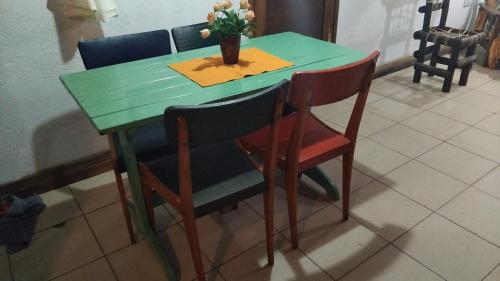 una mesa verde con 4 sillas y un jarrón con flores en Cabaña giardino, en Villa Giardino