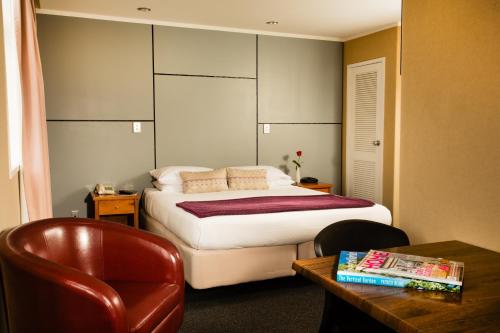 a bedroom with a bed and a chair and a table at The Grosvenor Hotel in Timaru