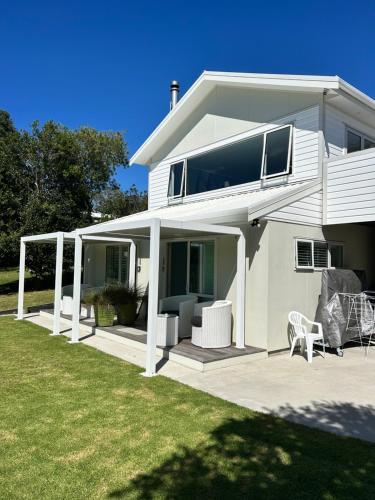 a white house with white chairs and a patio at Hahei Pavillion Guest House in Hahei