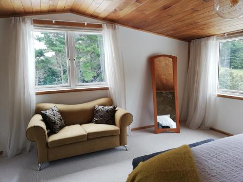 a bedroom with a couch and a mirror and windows at Old Mountain Road Retreat in Raglan