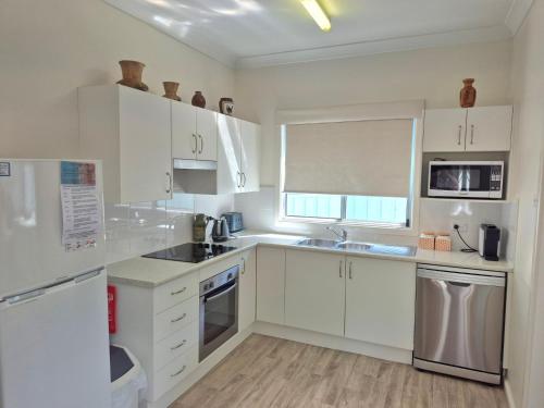 a white kitchen with white cabinets and a window at Shamrose Cottage - Huskisson in Huskisson