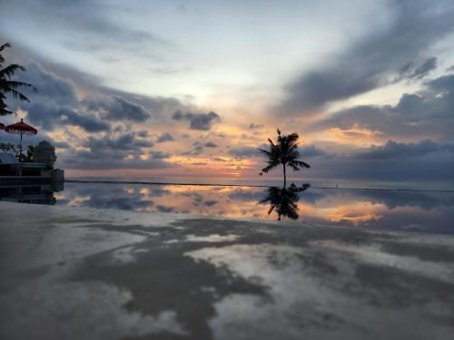 a sunset on a beach with a palm tree and the water at Villa Umbrella Lombok in Senggigi 