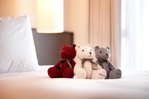 three stuffed teddy bears sitting on a bed at Shilla Stay Cheonan Asan - Samsung Display City in Cheonan