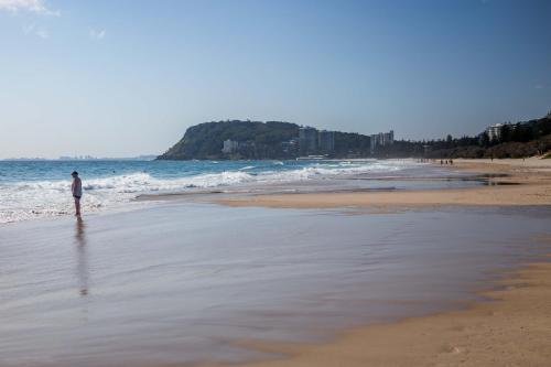 a man standing on a beach near the ocean at Solnamara Beachfront Apartments in Gold Coast