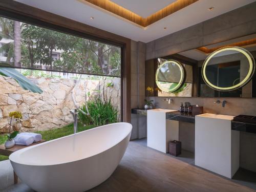 a bathroom with a tub and a large window at Pullman Lombok Merujani Mandalika Beach Resort in Kuta Lombok
