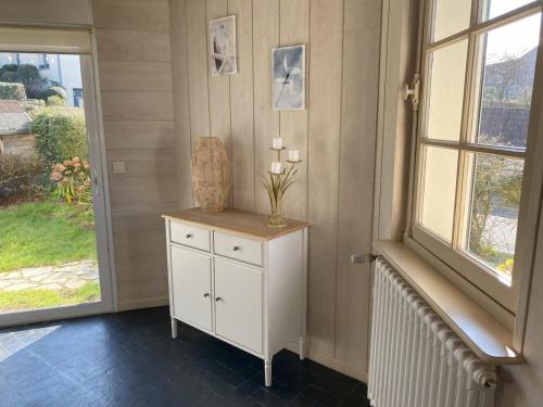 a room with a white cabinet with a vase and a window at Le Moulin in Saint-Pair-sur-Mer