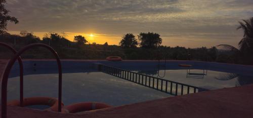a swimming pool with a sunset in the background at Gokul farm house in Sasan Gir
