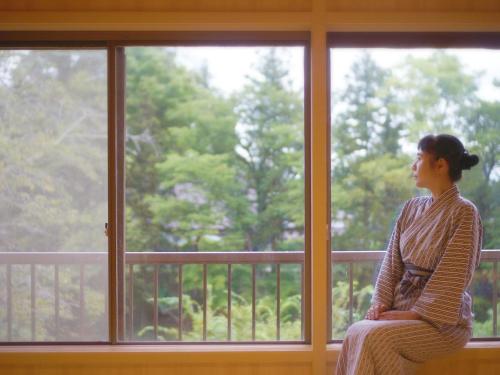 a woman sitting on a window sill looking outside at 厳美渓温泉いつくし園 in Itsukushi