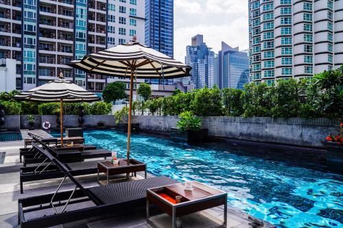 a swimming pool with tables and umbrellas in a city at Mövenpick Hotel Sukhumvit 15 Bangkok in Bangkok