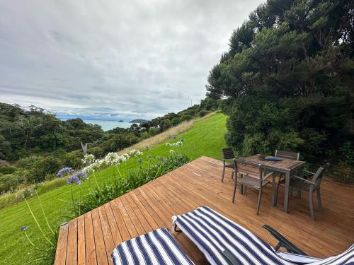 a patio with a table and chairs on a wooden deck at Aroha A-Frames - Bush & Beach Retro Retreat in Coromandel Town