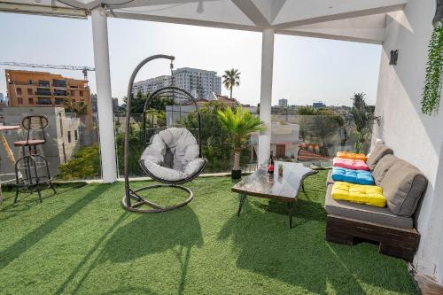 a patio with a couch and a swing on a roof at הפנטהאוז של תל אביב - דירות סטודיו מהממות ופנטהאוז משגע עם ג'קוזי פרטי! in Tel Aviv