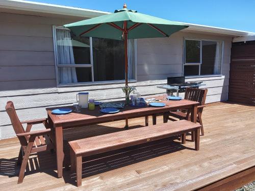 a wooden table and bench with an umbrella on a deck at The Willow - Hanmer Springs Holiday Home in Hanmer Springs