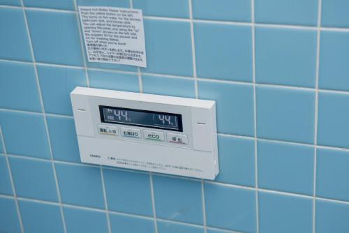 a digital clock on a blue tiled bathroom wall at Benton Guesthouse, Private Nostalgic Showa-era House, former "Akiya" in Imabari