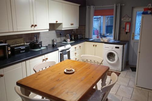a kitchen with a wooden table and white cabinets at Cosy Cottage- Sleeps 4 Free Parking & Golf Nearby in Buncrana