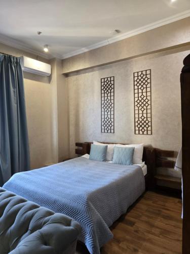 a bedroom with a bed with blue sheets and two windows at Saraishyq Hotel in Almaty