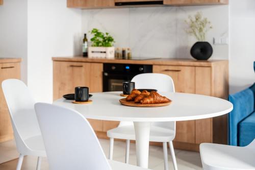 a white table with white chairs and a plate of croissants at Apartamenty Fuzja - Komfortowe Mieszkania Blisko Centrum Łodzi Garaż in Łódź