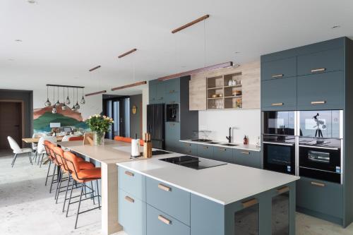 une cuisine avec des armoires bleues et un îlot avec des chaises orange dans l'établissement L'Odyssée du Val - Vue mer, à Pléneuf-Val-André