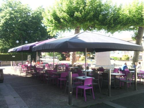 a patio area with tables, chairs and umbrellas at Hôtel du Centre in Soustons
