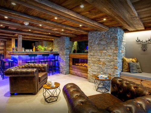 Il comprend un salon doté d'un mobilier en cuir et d'une cheminée en pierre. dans l'établissement Chalet Colombine - OVO Network, à Les Villards-sur-Thônes