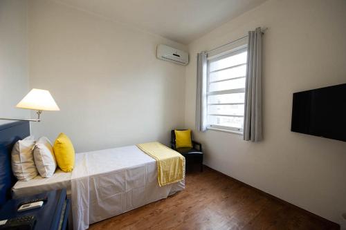 a bedroom with a bed with yellow pillows and a television at Hotel Normandie in Sao Paulo