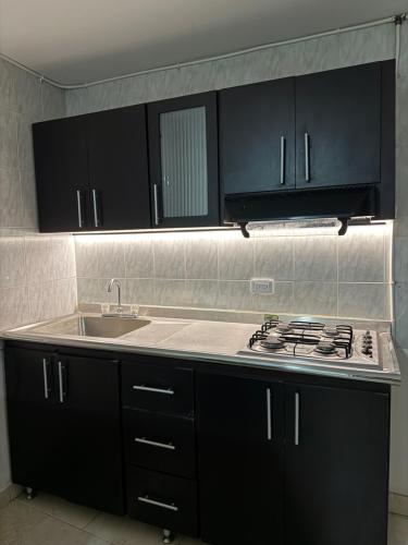 a kitchen with black cabinets and a stove and a sink at DHG Apartahotel in Pereira